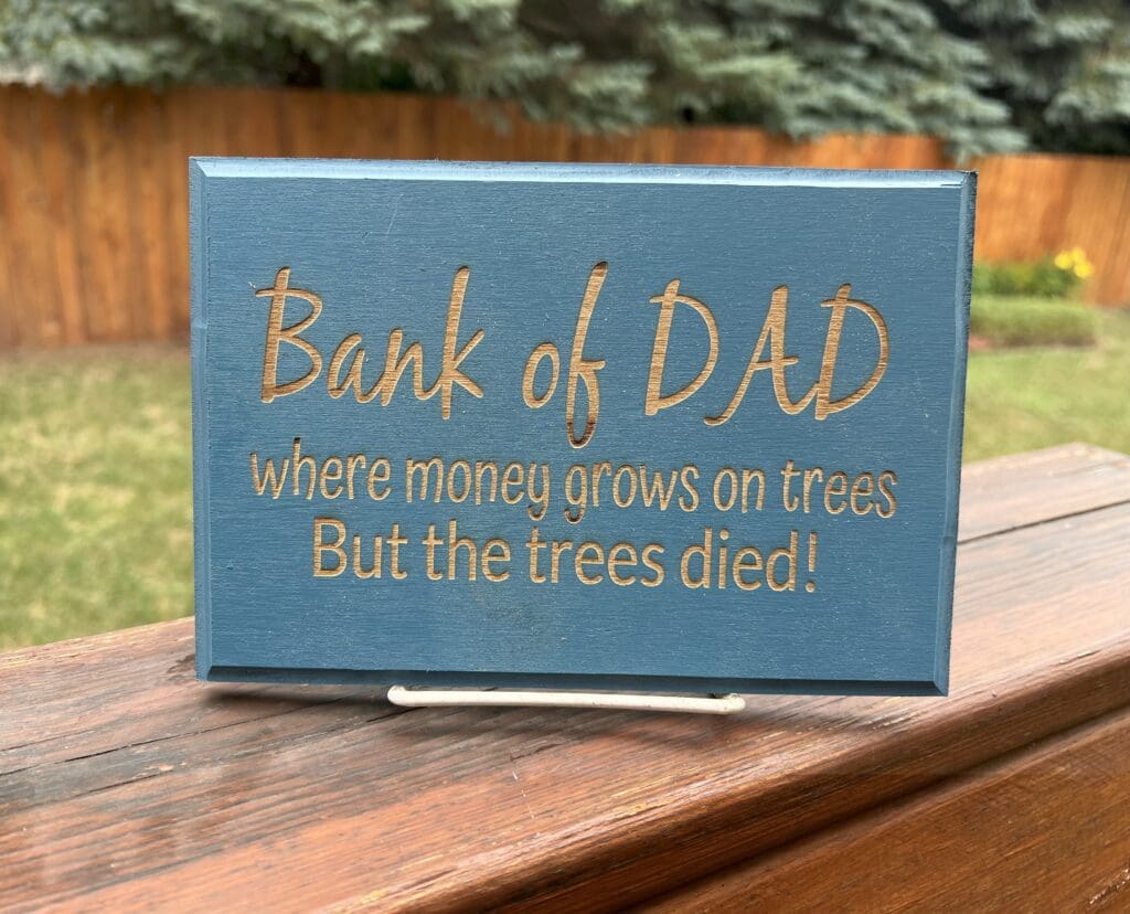 A humorous wooden plaque about a 'Bank of Dad' with a joke about trees dying.