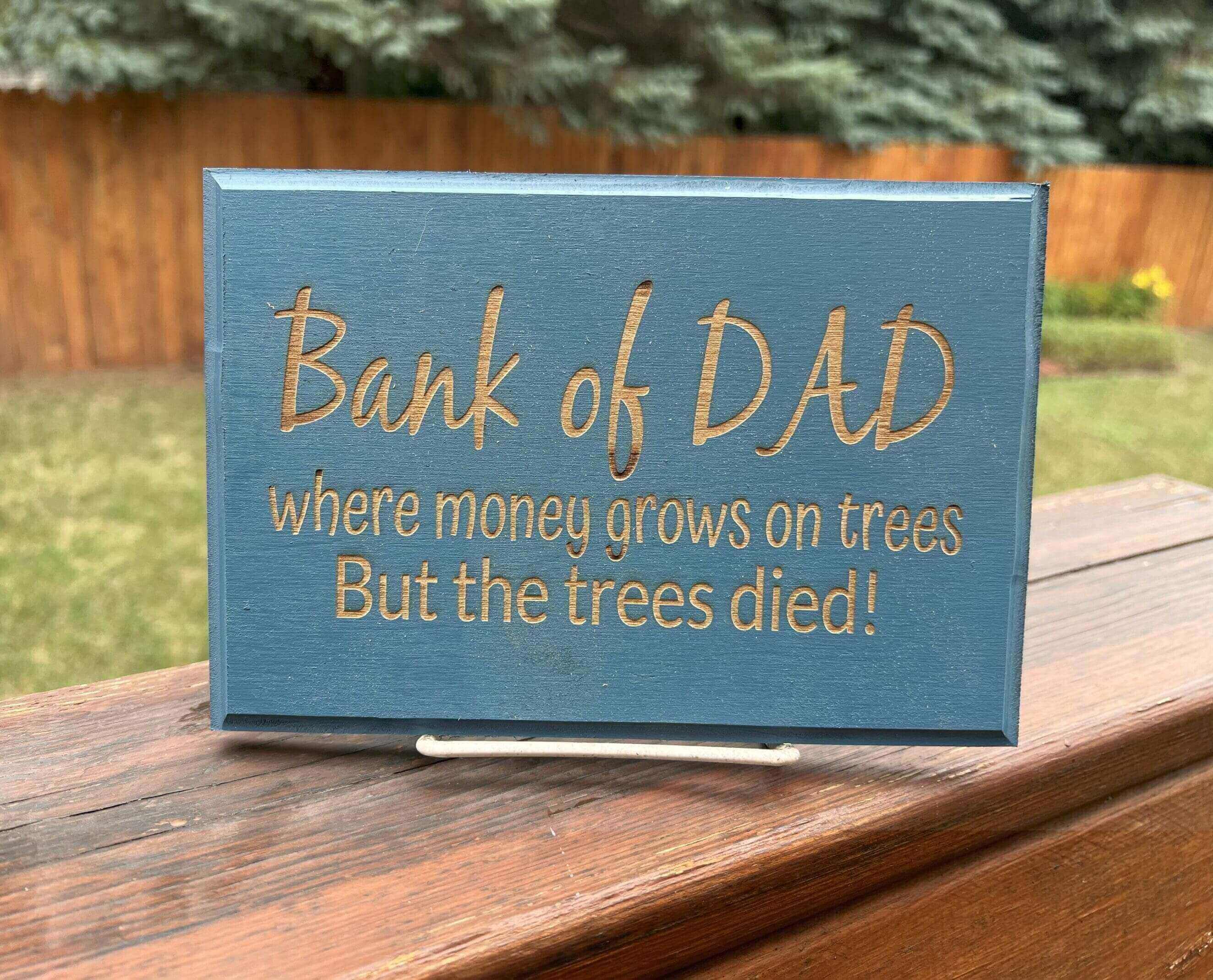 A humorous wooden plaque about a 'Bank of Dad' with a joke about trees dying.