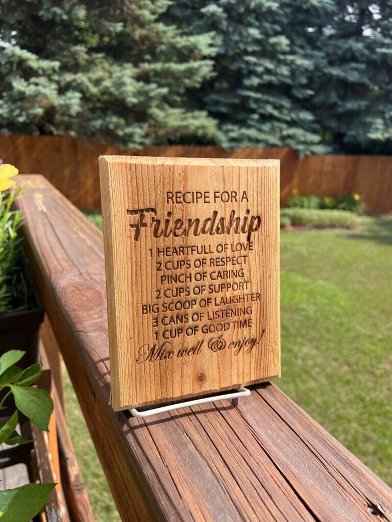 Wooden plaque with a Friendship recipe engraved, placed outdoors.